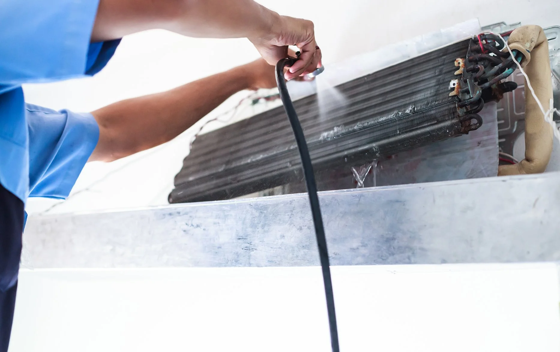 close-up of an HVAC technician using a hose to clean the condenser coils on an air conditioning unit during a professional tune-up