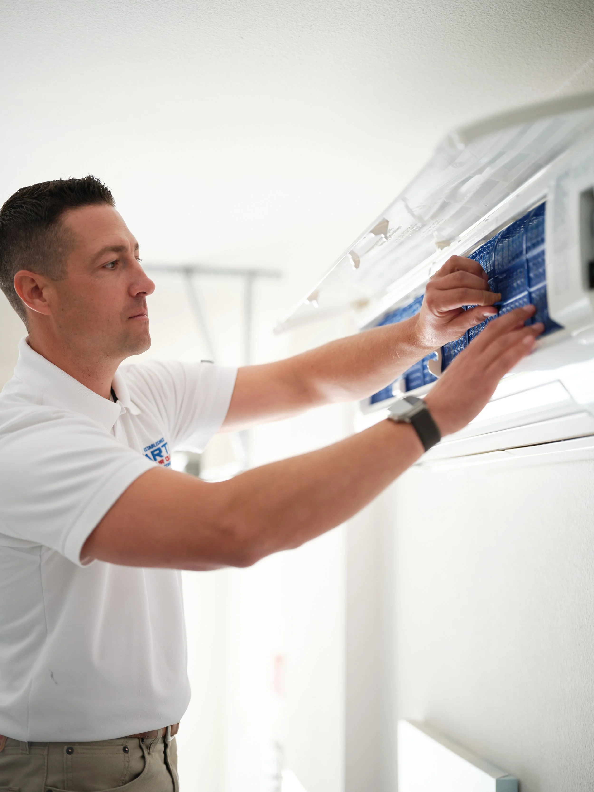 HVAC technician replacing air filter in wall-mounted air conditioning unit during spring maintenance