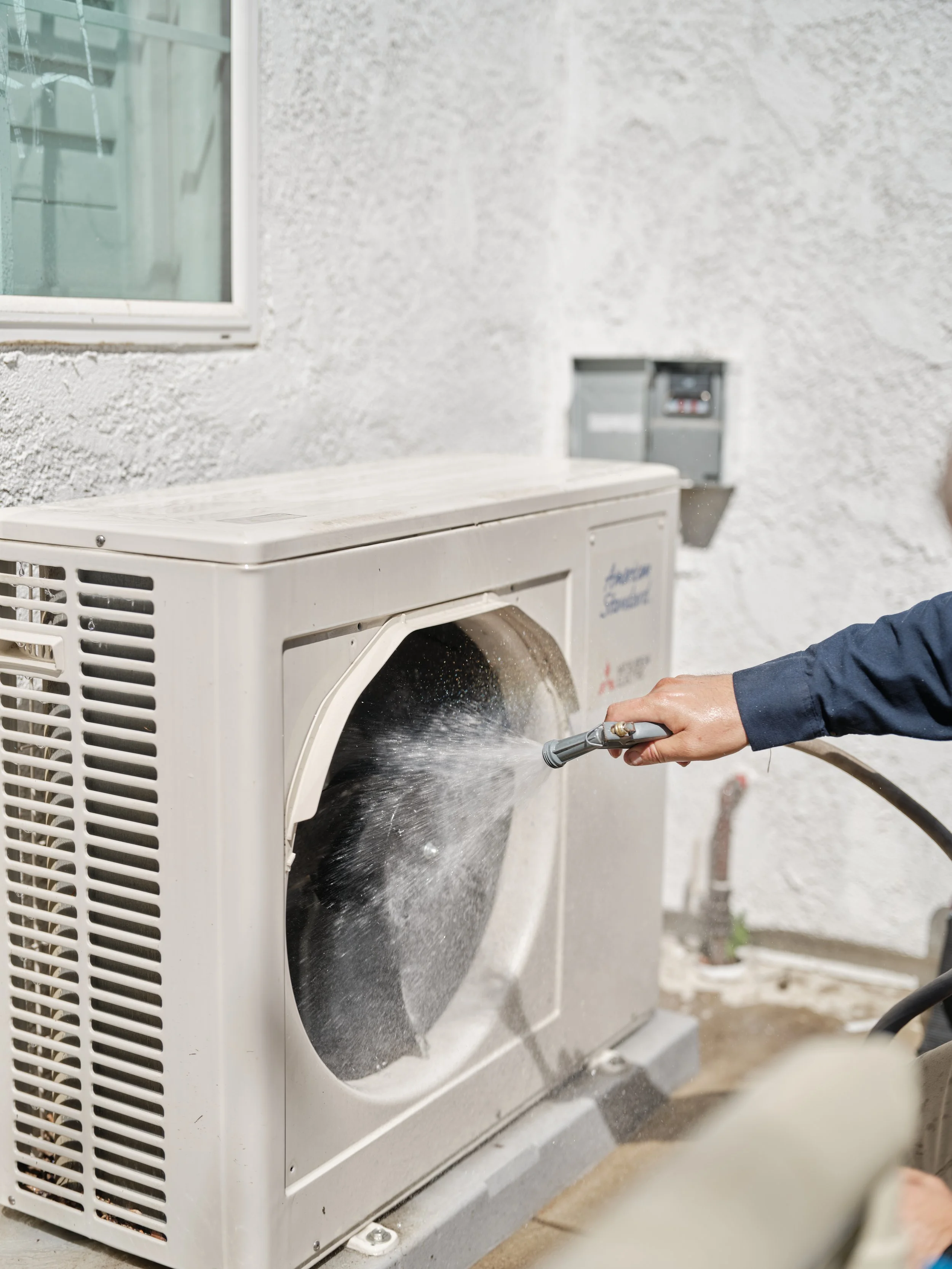 Professional technician cleaning air conditioning condenser coils with pressure washer in Mission Viejo