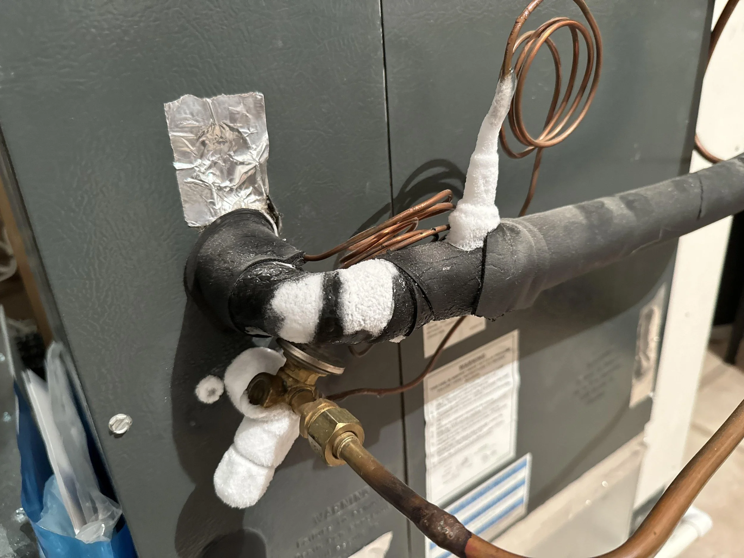 Ice buildup on AC refrigerant lines near an indoor air handler caused by a frozen evaporator coil