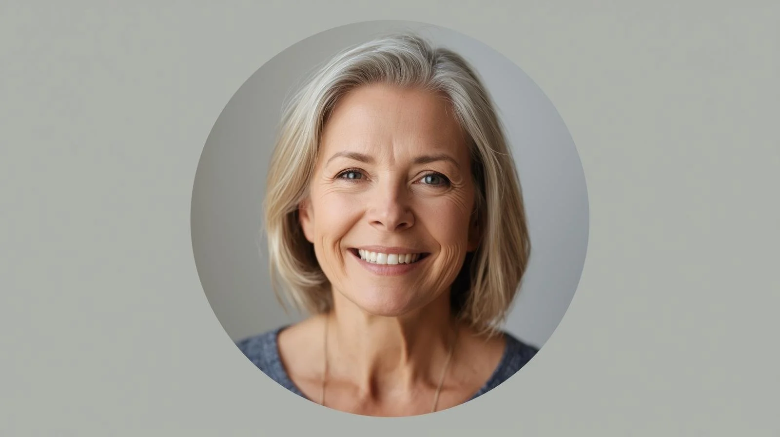 A woman with short, light brown hair and glasses smiling at a restaurant table with a drink and menu in front of her.