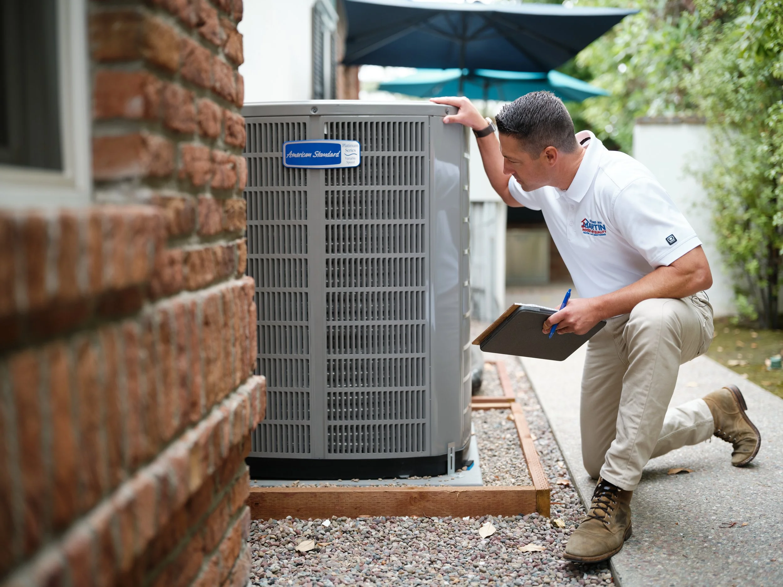 J Martin HVAC technician inspecting outdoor air conditioning unit during maintenance visit in Orange County