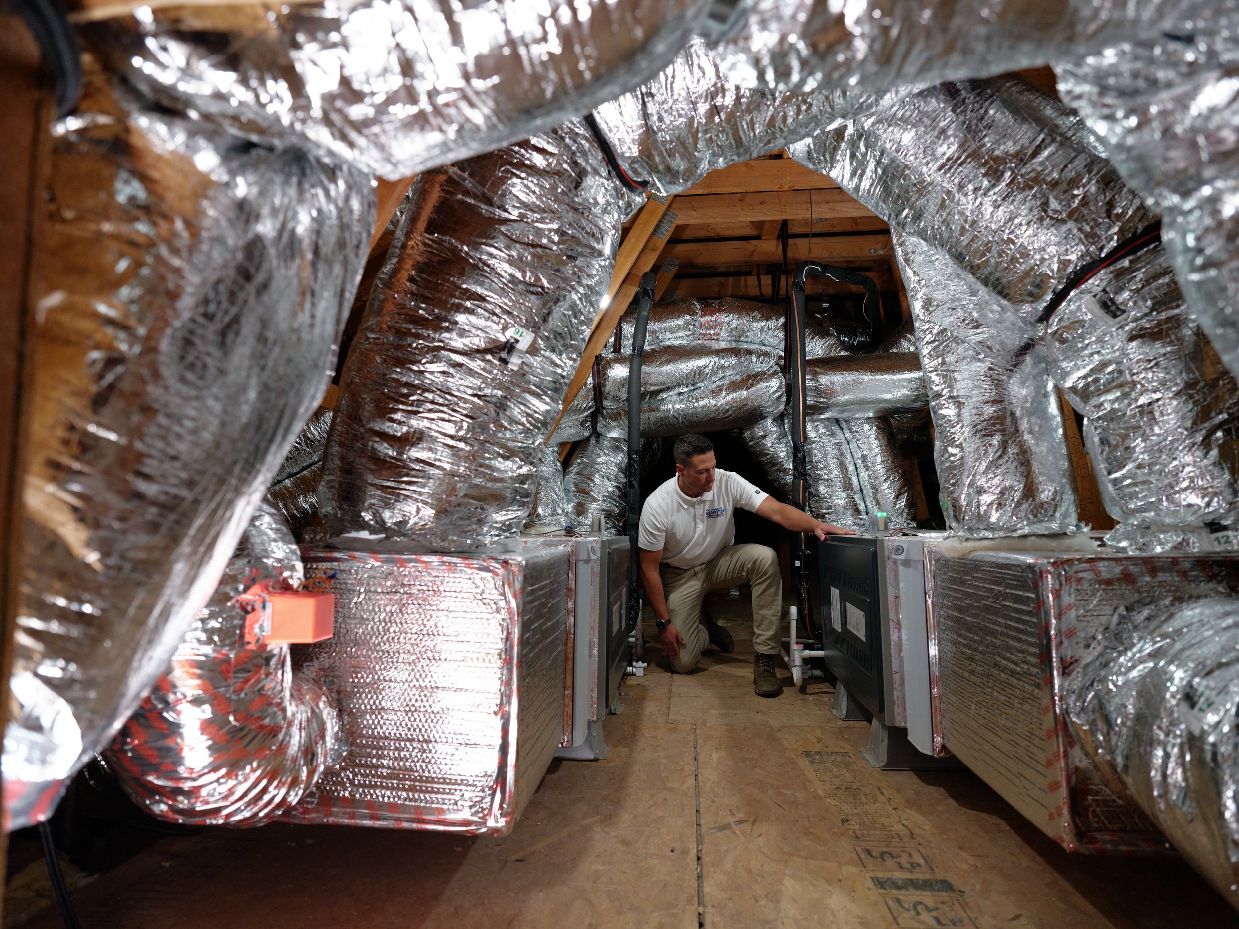 technician checking residential HVAC ductwork and air handler units inside attic space.