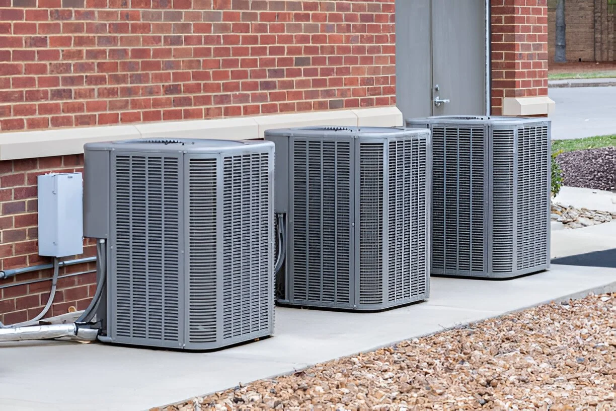 Multiple outdoor central air conditioner condenser units installed beside a building