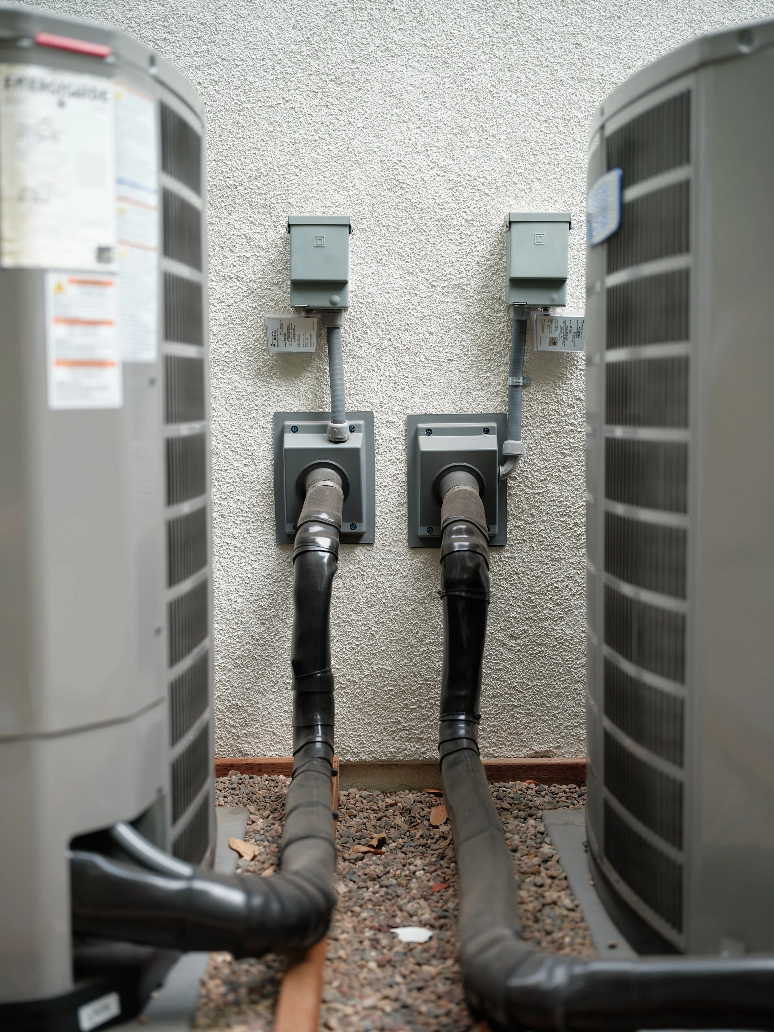 side-by-side heat pump outdoor unit installation showing professional code-compliant electrical work, proper disconnects, and clean conduit installation on residential property