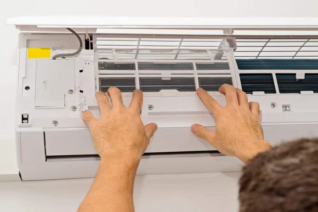 homeowner removing filter from mini-split HVAC unit for fall maintenance