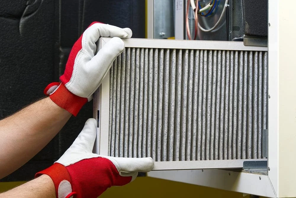 technician removing heavily clogged dirty furnace filter during fall HVAC maintenance