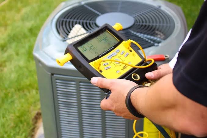 HVAC technician using a digital refrigerant pressure gauge to diagnose an outdoor air conditioning condenser unit