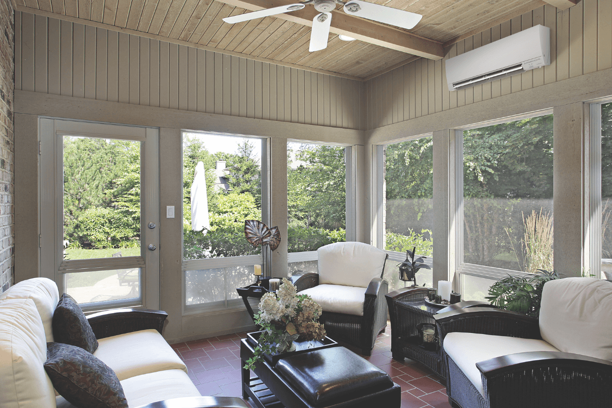 ductless mini split air handler mounted above wicker furniture in a bright sunroom living space
