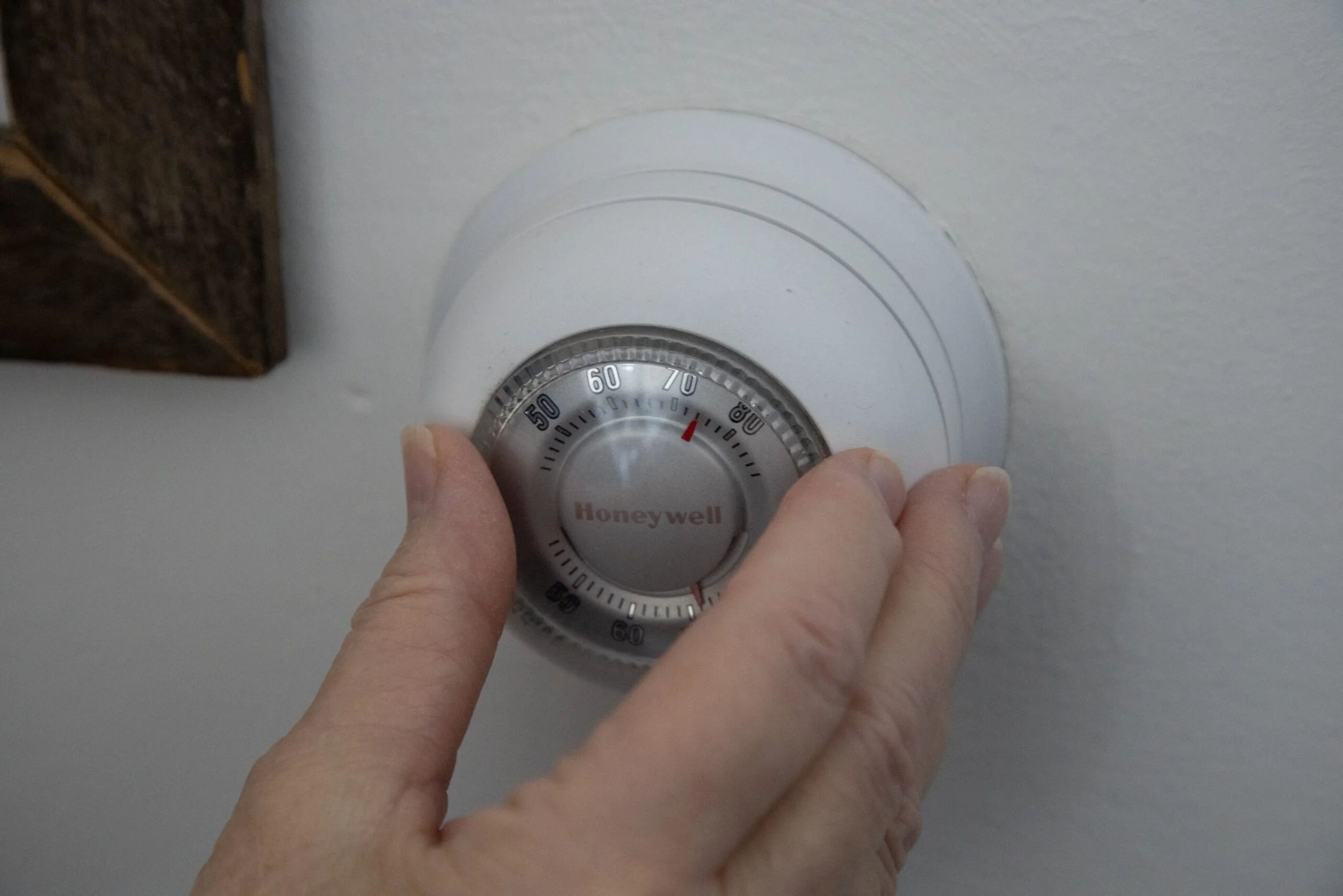 Hand adjusting a Honeywell wall thermostat to change home temperature setting