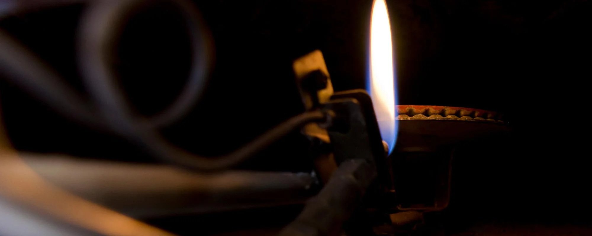 Close-up of a furnace pilot light flame burning inside an older gas furnace burner assembly