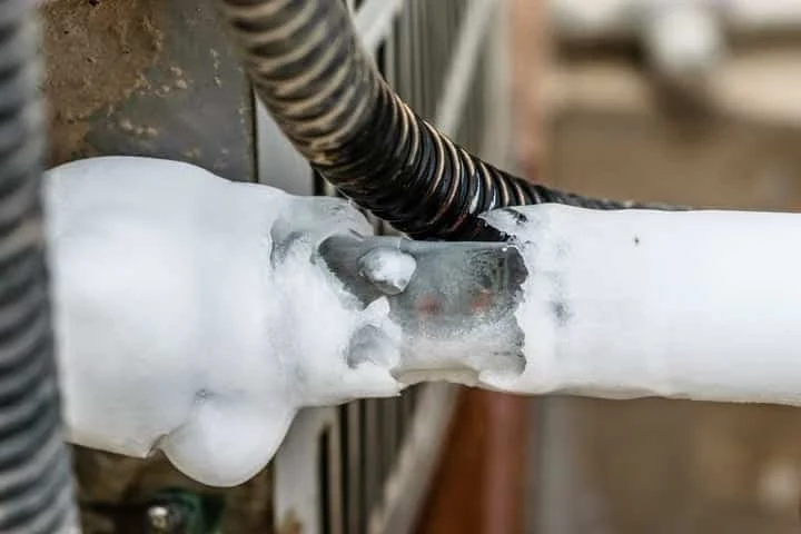 Frozen refrigerant line on an outdoor AC condenser unit, a warning sign of low refrigerant or restricted airflow common in aging Fullerton tract homes that requires immediate professional service to prevent compressor damage