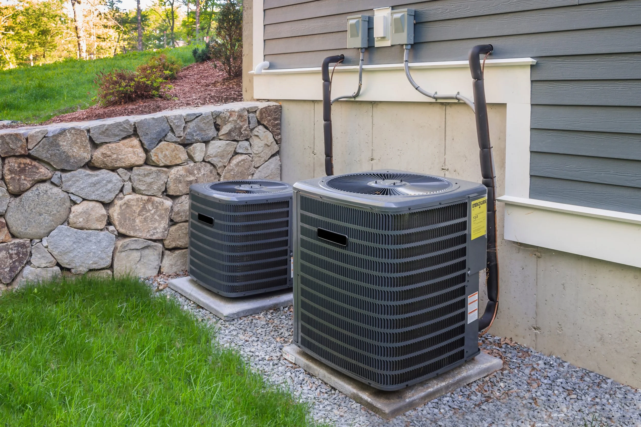 two HVAC outdoor condenser units installed on concrete pads beside a residential home exterior with EnergyGuide label visible on the front unit