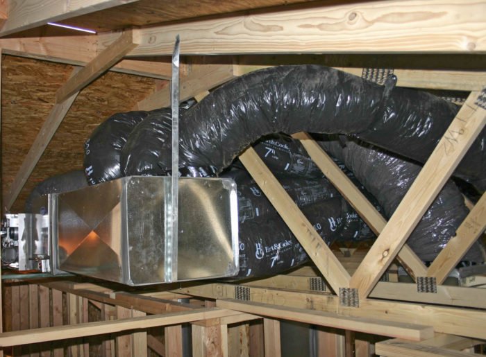 flexible ductwork and metal air handler box installed in a residential attic with wood truss framing for a two-story home HVAC system