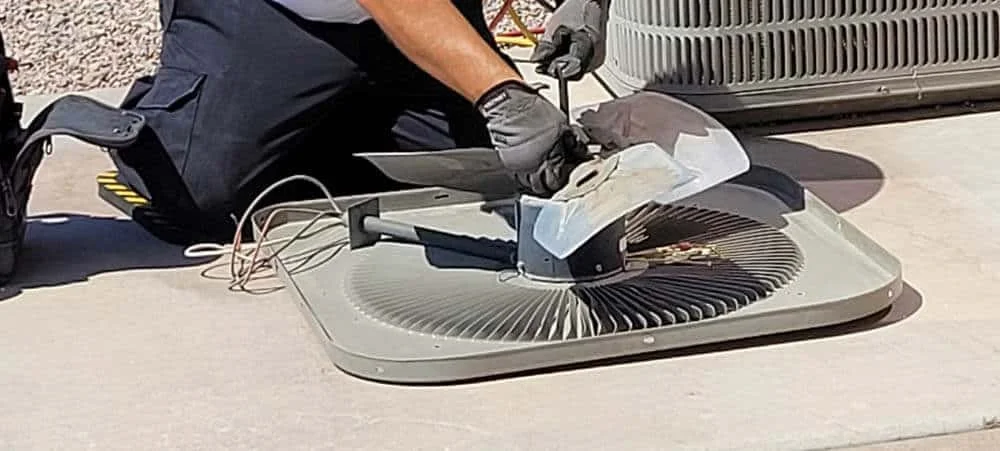 HVAC technician inspecting condenser fan blade during fall tune-up
