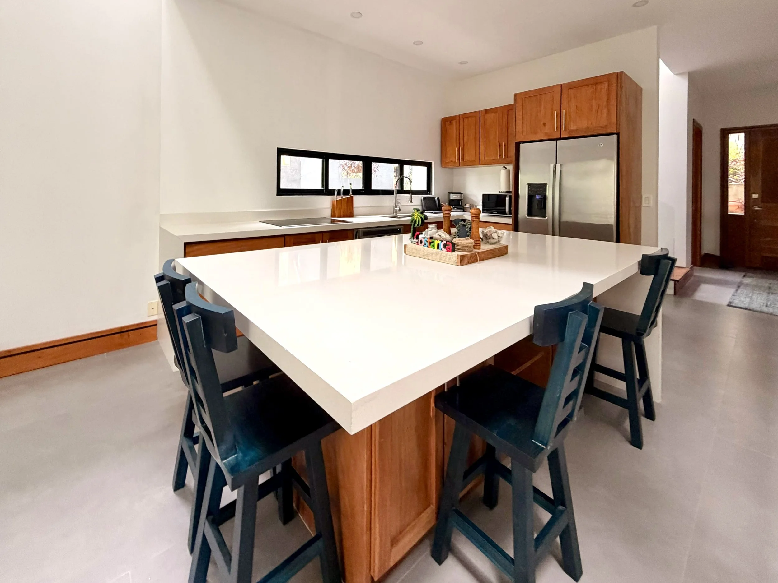 Casa Colina modern kitchen featuring a spacious white island, natural wood cabinetry and bar seating.