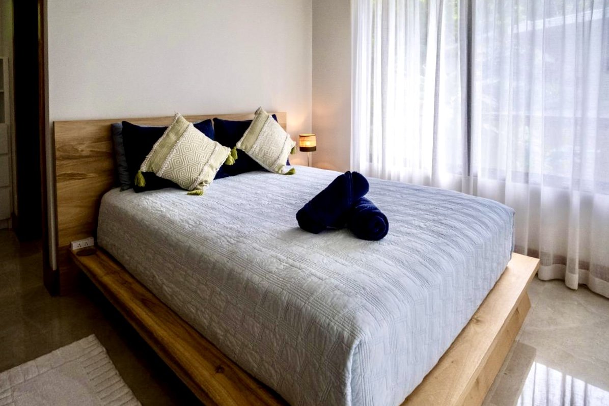 Bright furnished bedroom with wooden platform bed, soft white curtains and comfortable modern decor at House of Light in Paquera, Costa Rica