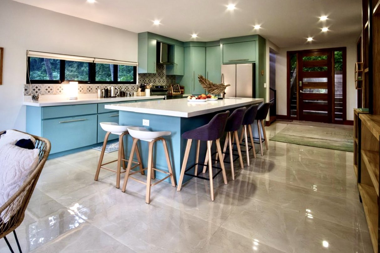 Contemporary kitchen with spacious white quartz island, soft green cabinetry, breakfast seating and tropical views at House of Light in Paquera