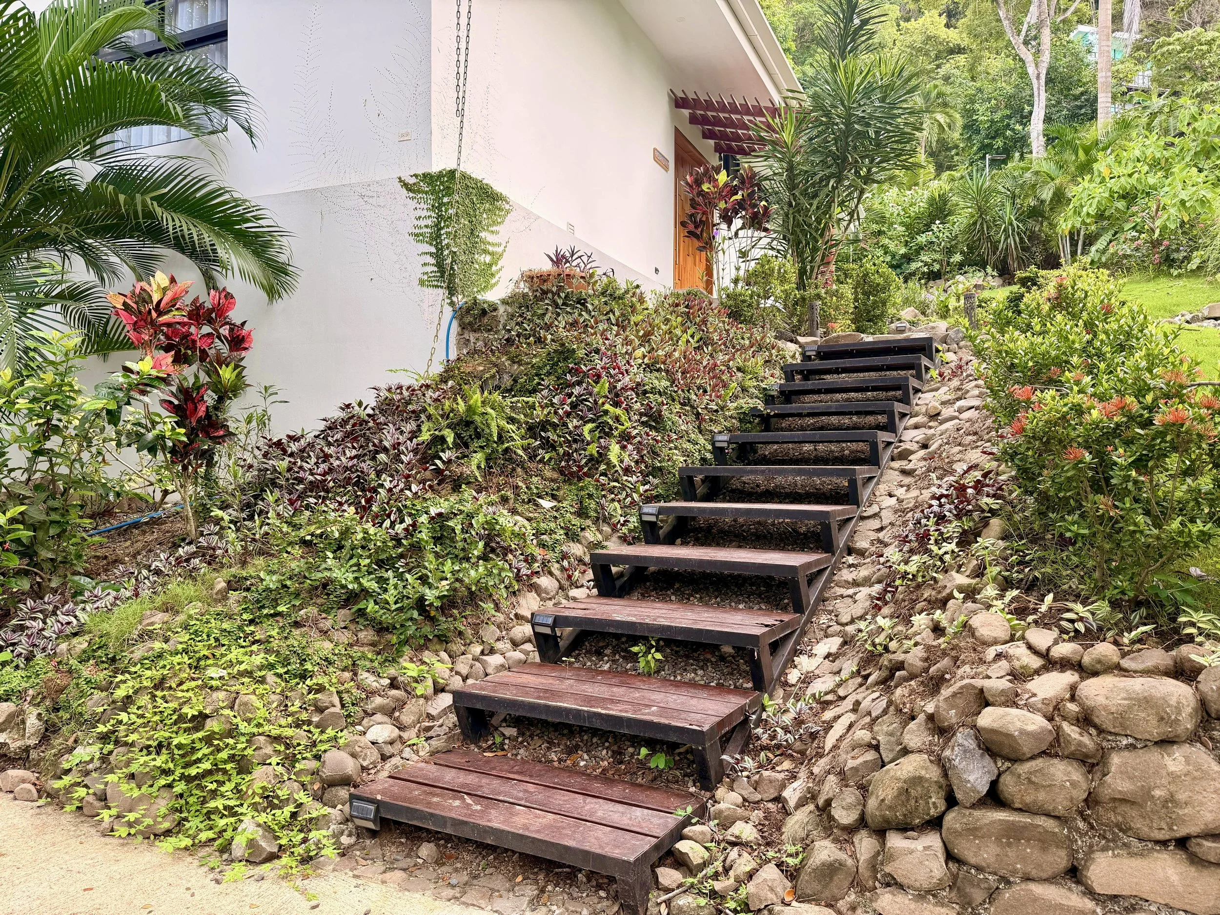 Casa Quantum landscaped garden pathway with wooden steps, natural stone edging and lush tropical plants.