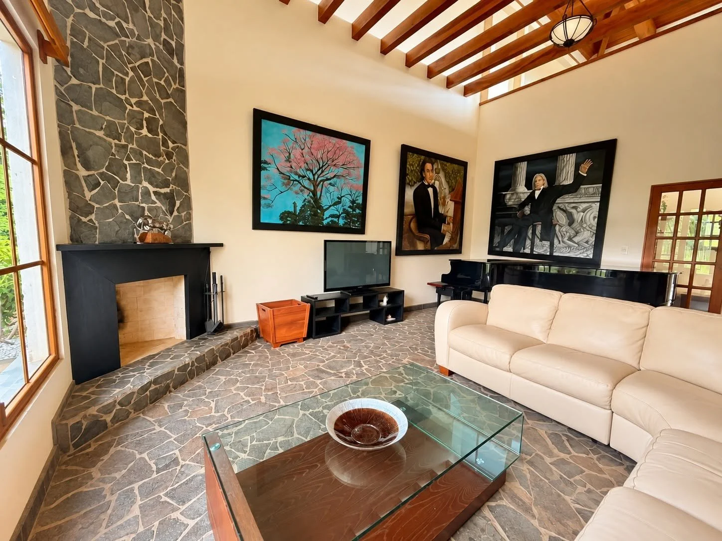 Spacious luxury living room featuring stone fireplace, grand piano and exposed wooden ceiling