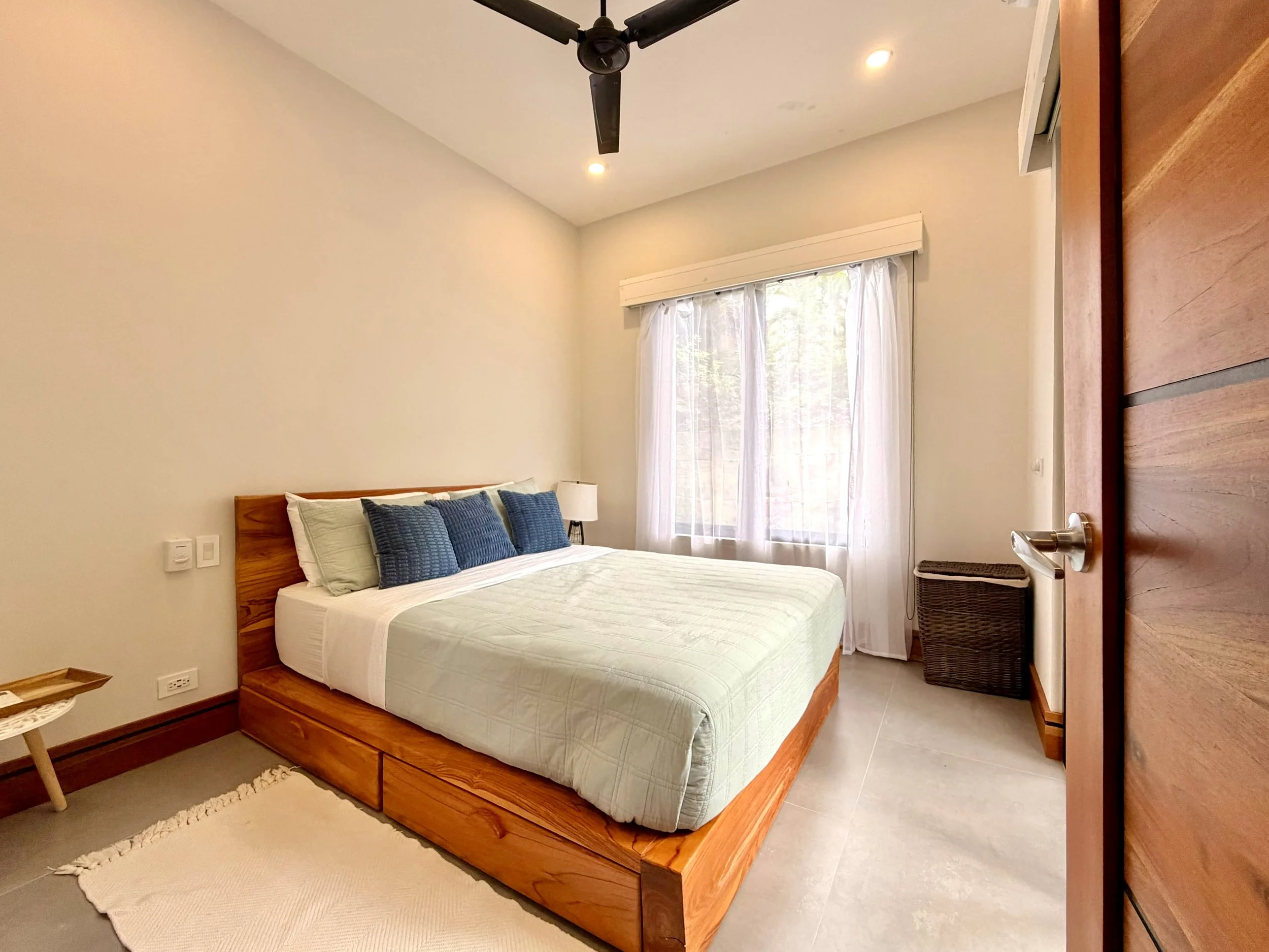 Casa Colina furnished bedroom with wooden platform bed, ceiling fan and large window with garden views.