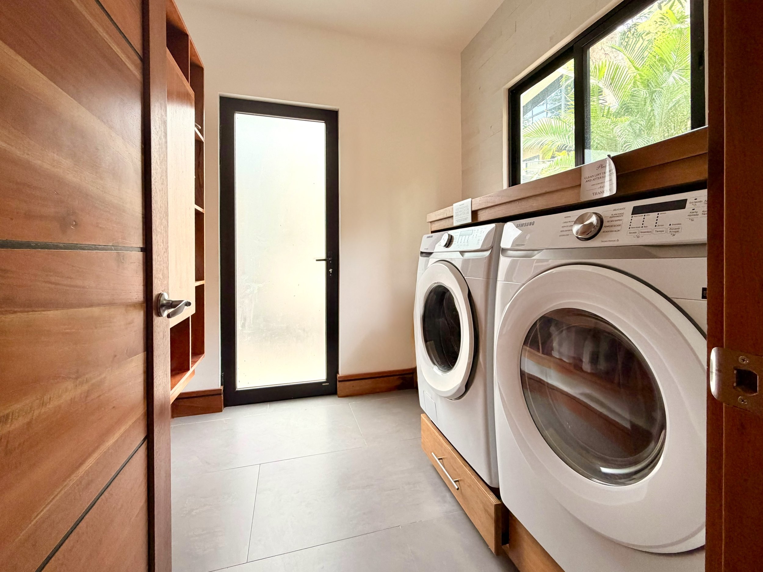 Casa Colina dedicated laundry room with front-loading washer and dryer, wooden cabinetry and natural light.