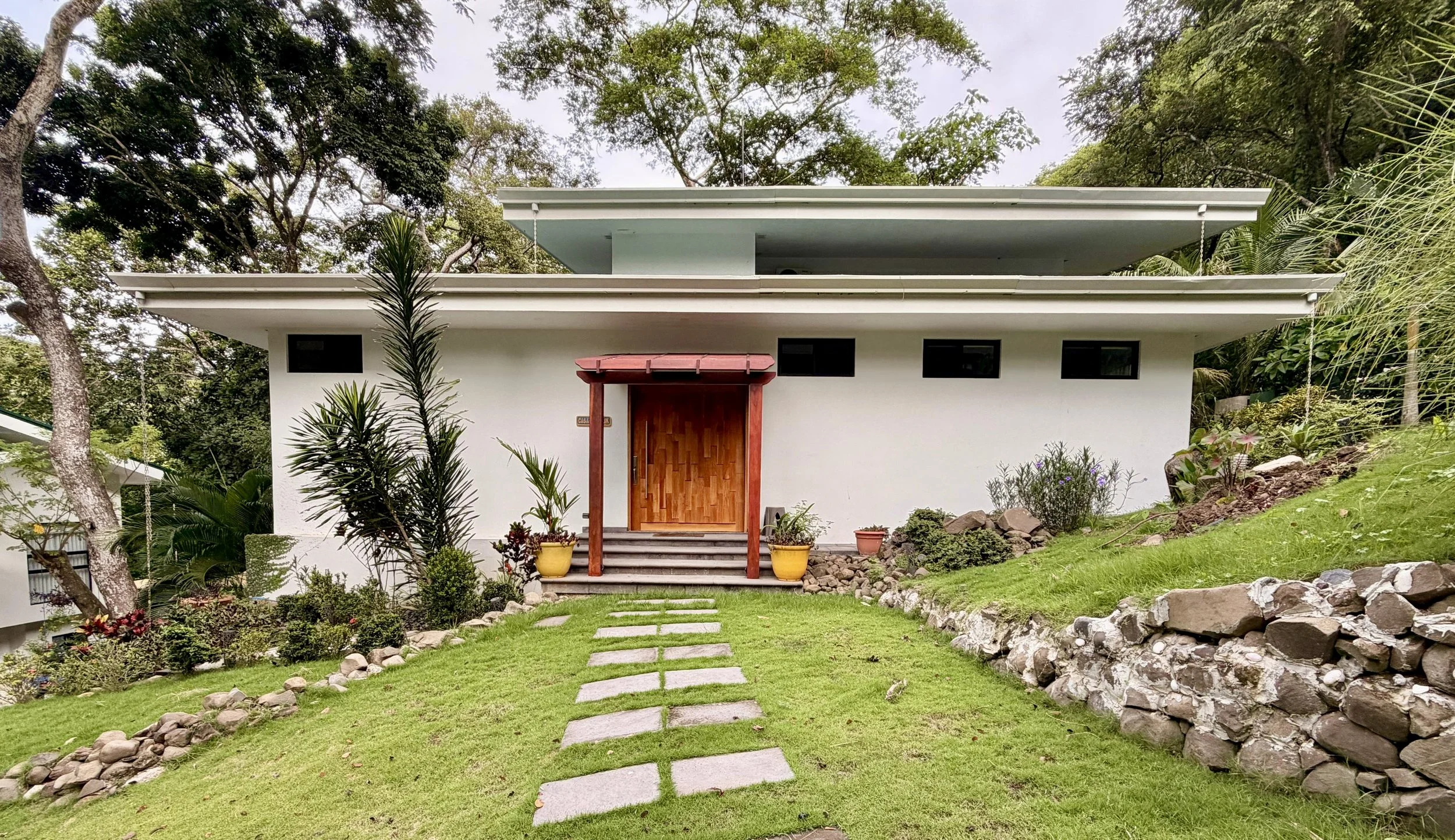 Casa Quantum main entrance with wooden front door, stone pathway and landscaped tropical garden.