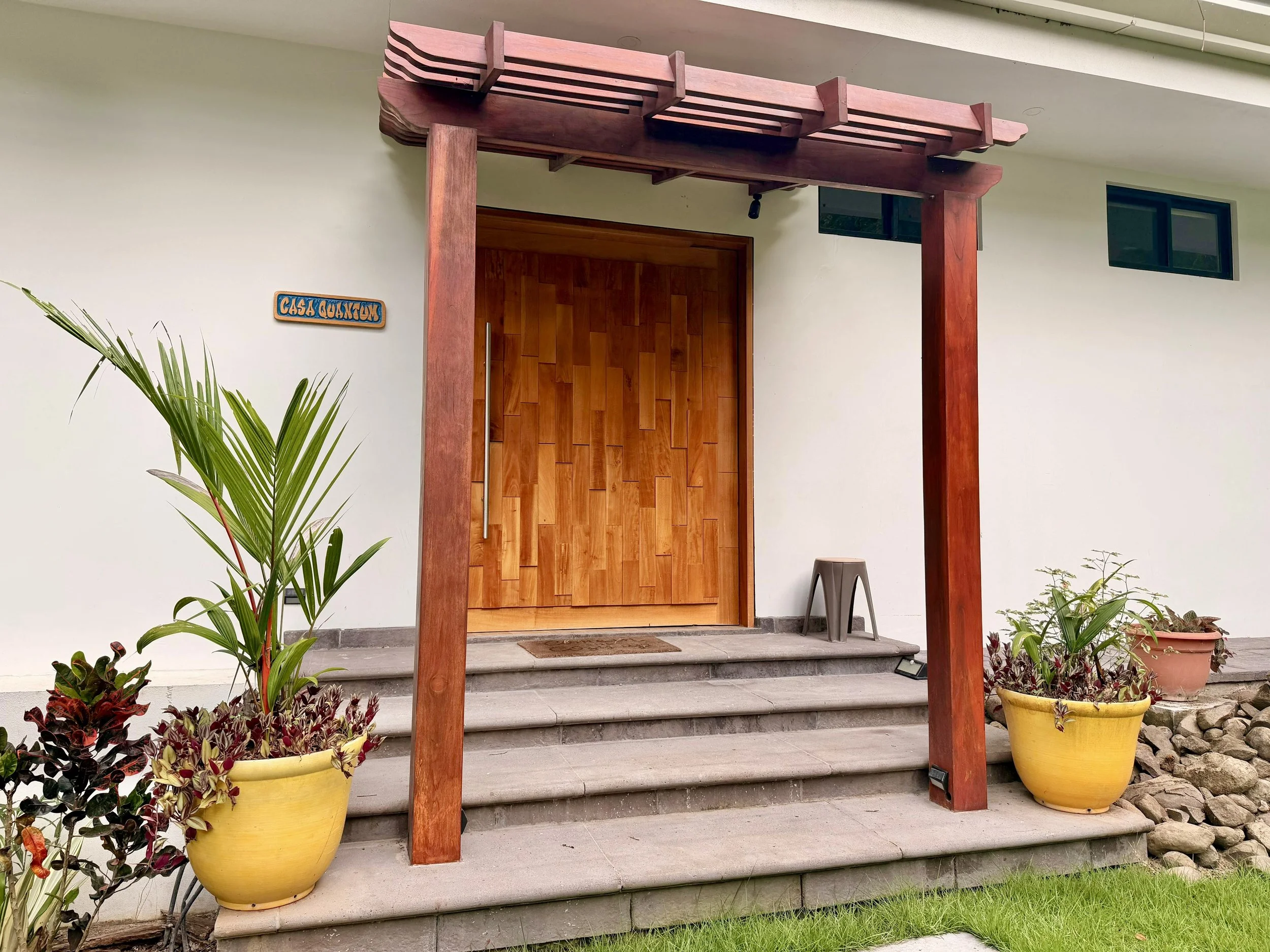 Casa Quantum covered entrance with natural wood front doors, timber posts and tropical potted plants.