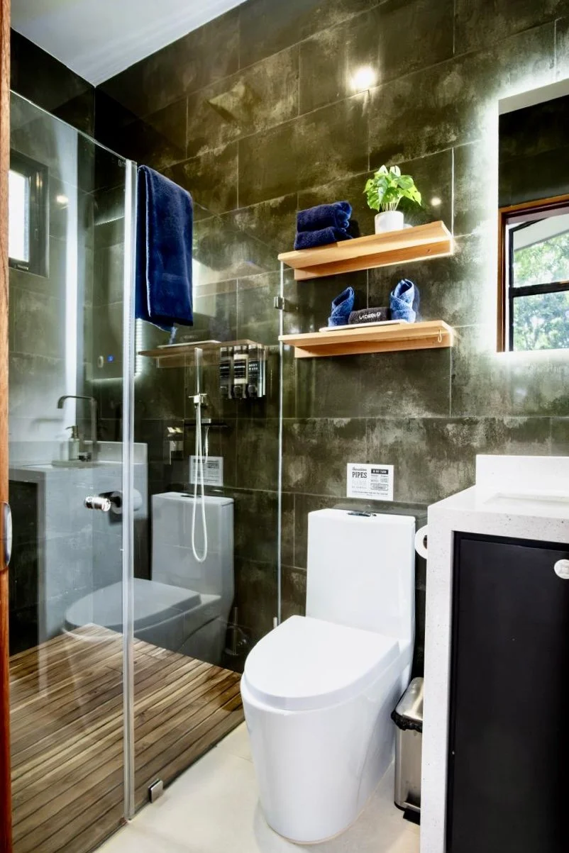 Contemporary bathroom with charcoal wall tiles, glass-enclosed walk-in shower and floating wooden shelves at House of Light in Paquera, Costa Rica