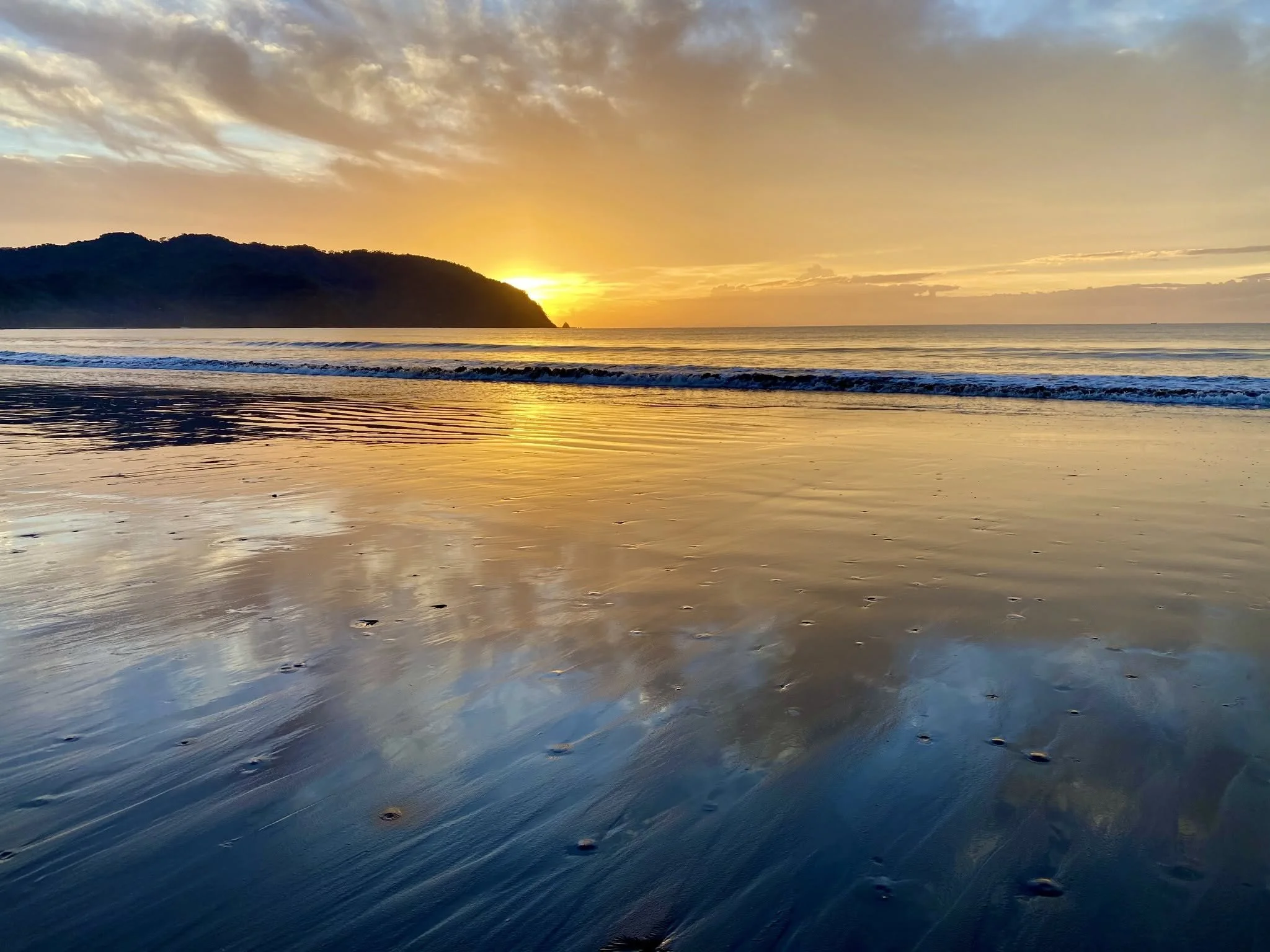 Golden sunset reflecting across the wet sand and Pacific Ocean at Tambor Beach, Costa Rica.