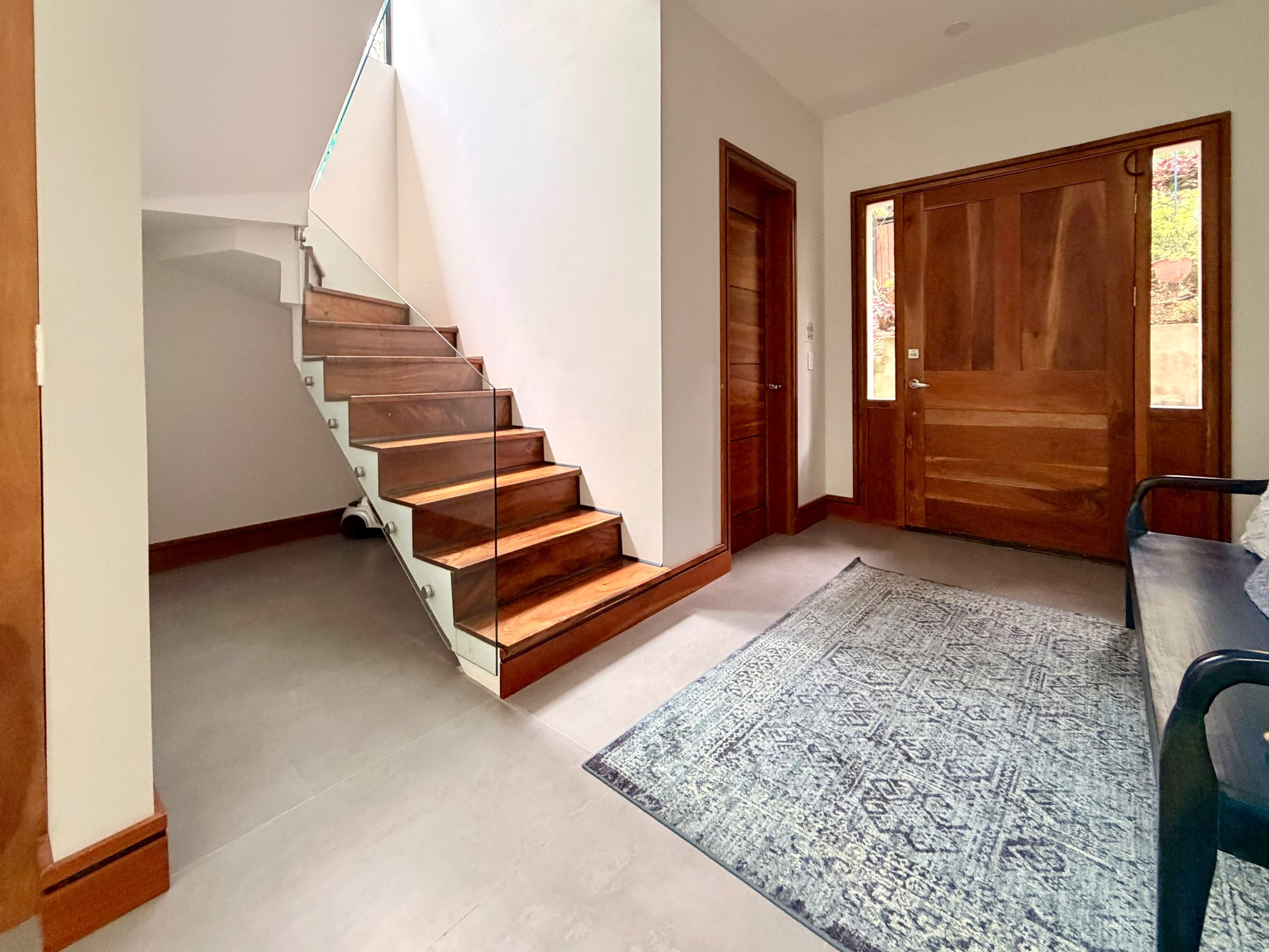 Casa Colina entrance foyer with wooden staircase, natural wood front door and contemporary tropical home design.