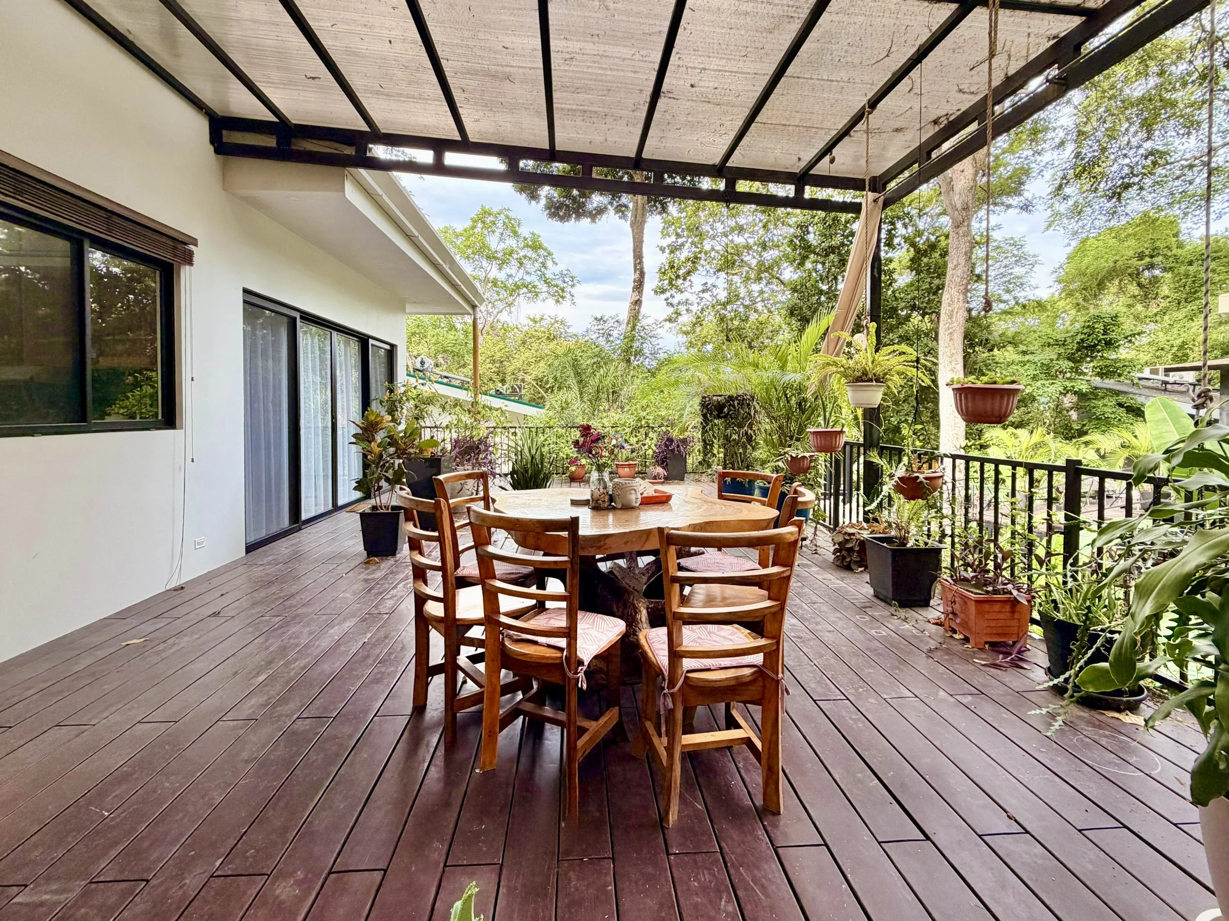 Casa Quantum spacious covered wooden terrace with outdoor dining table and tropical garden views.