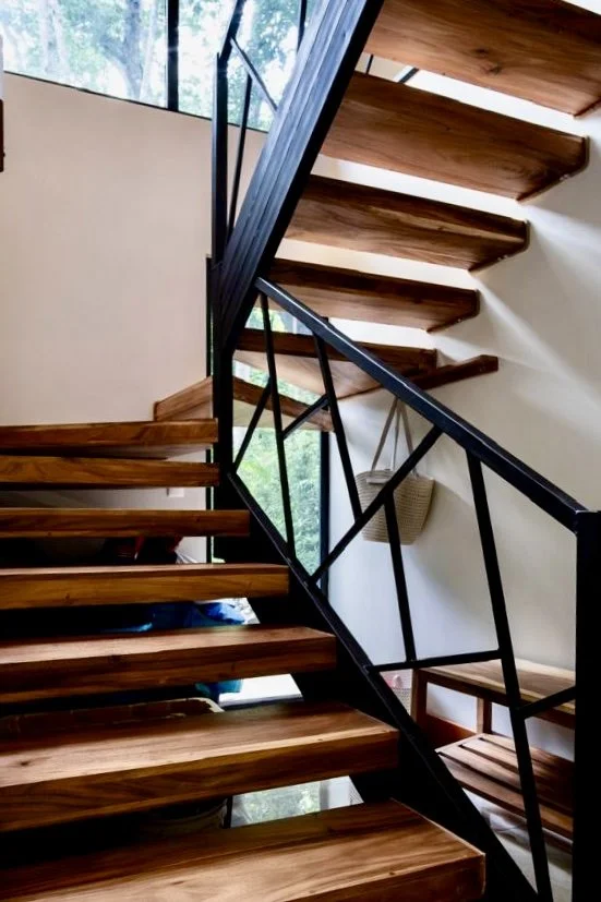 Contemporary open wooden staircase with black metal railings and natural light at House of Light in Paquera, Costa Rica