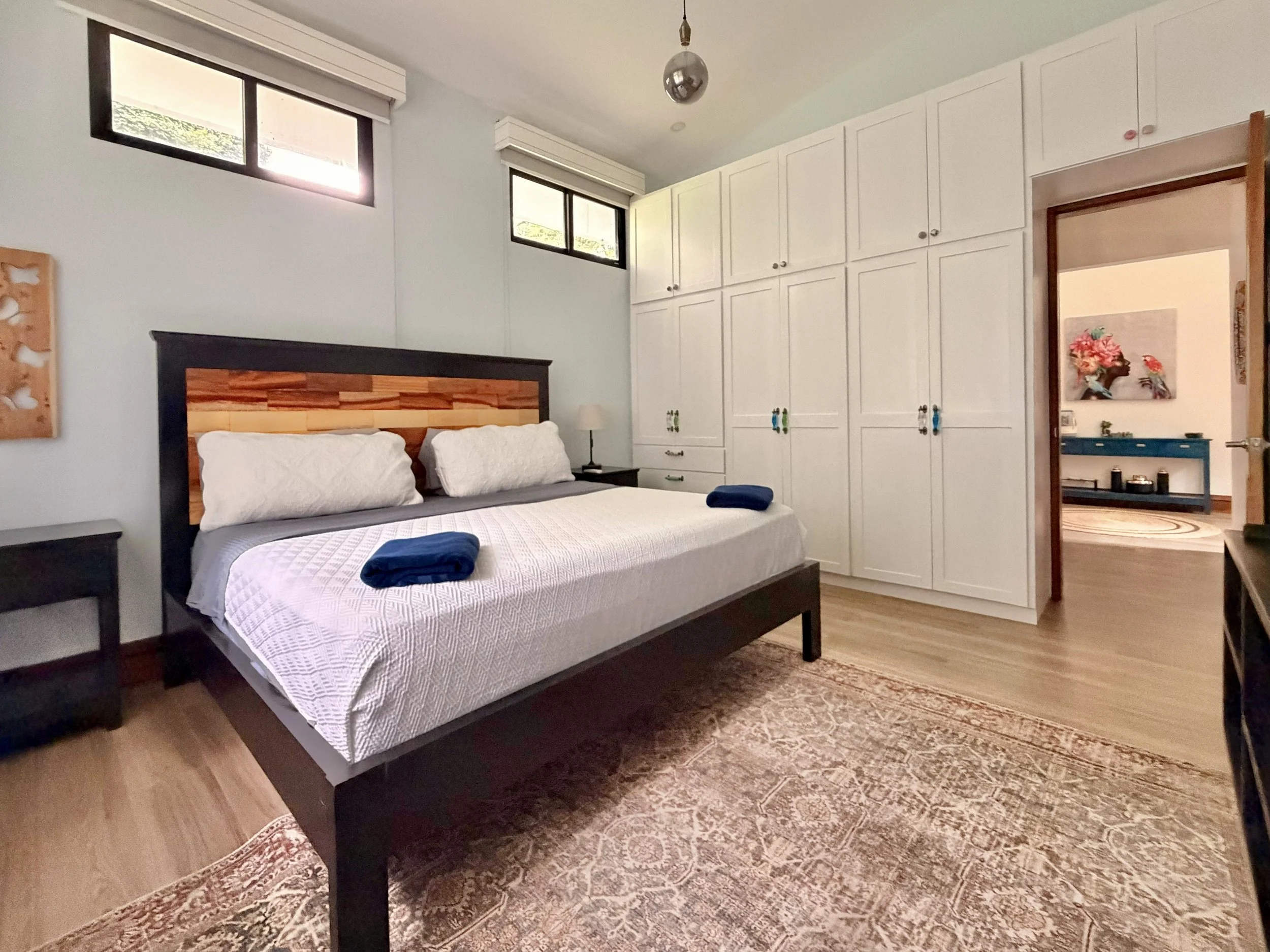 Casa Quantum bright guest bedroom with wooden bed frame, built-in white wardrobes and air-conditioning.
