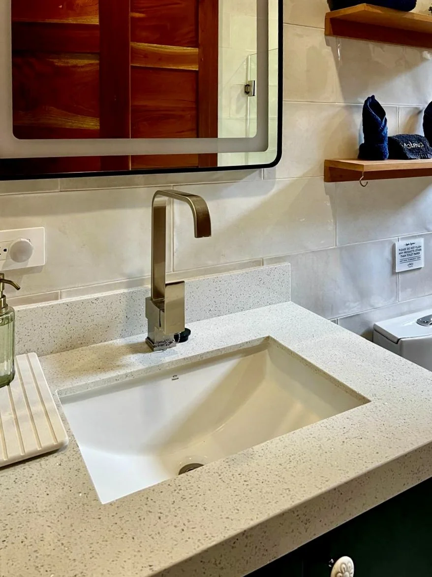 Contemporary bathroom vanity with white countertop, rectangular sink, brushed-metal faucet and wooden shelving at House of Light in Paquera, Costa Rica