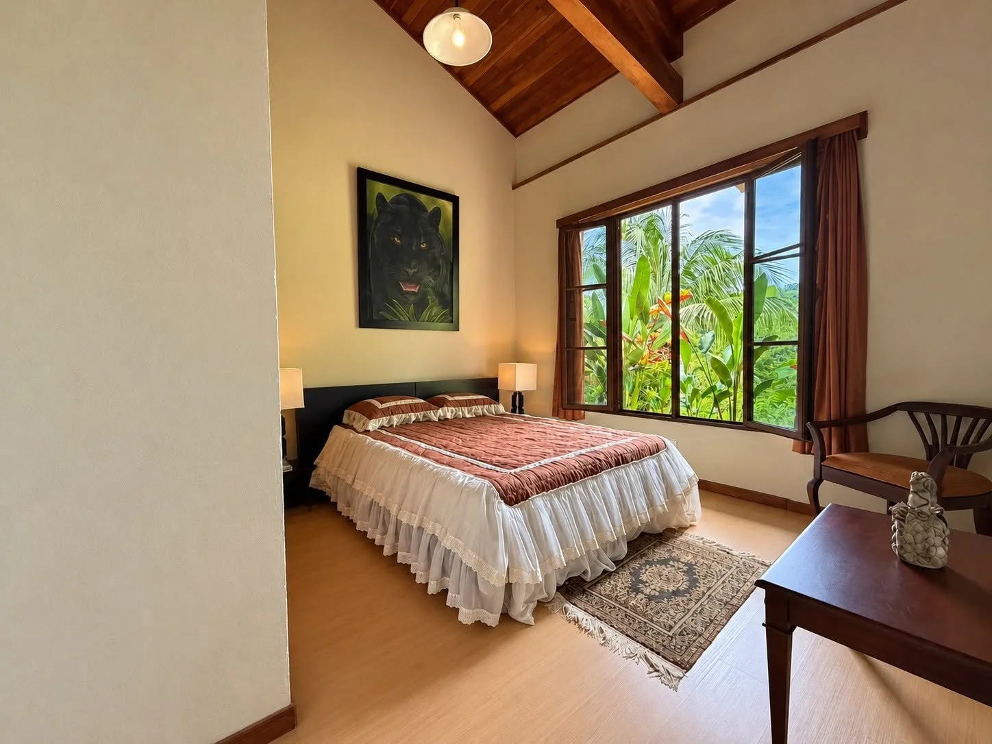 Bright guest bedroom with wood flooring and tropical greenery outside the window