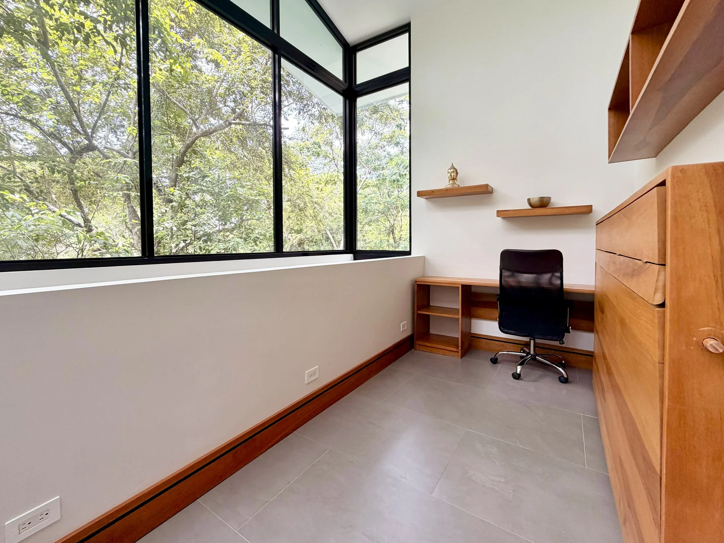 Casa Colina flexible home office and guest room with wooden Murphy bed and large corner windows overlooking tropical trees.