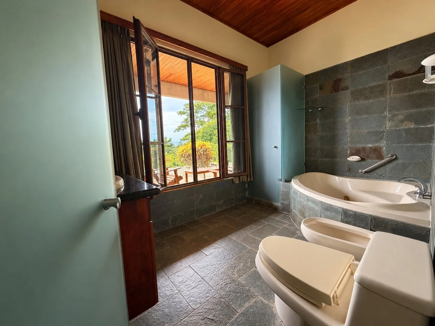 Spacious bathroom with bathtub, stone finishes and garden-facing windows at Finca Pamela