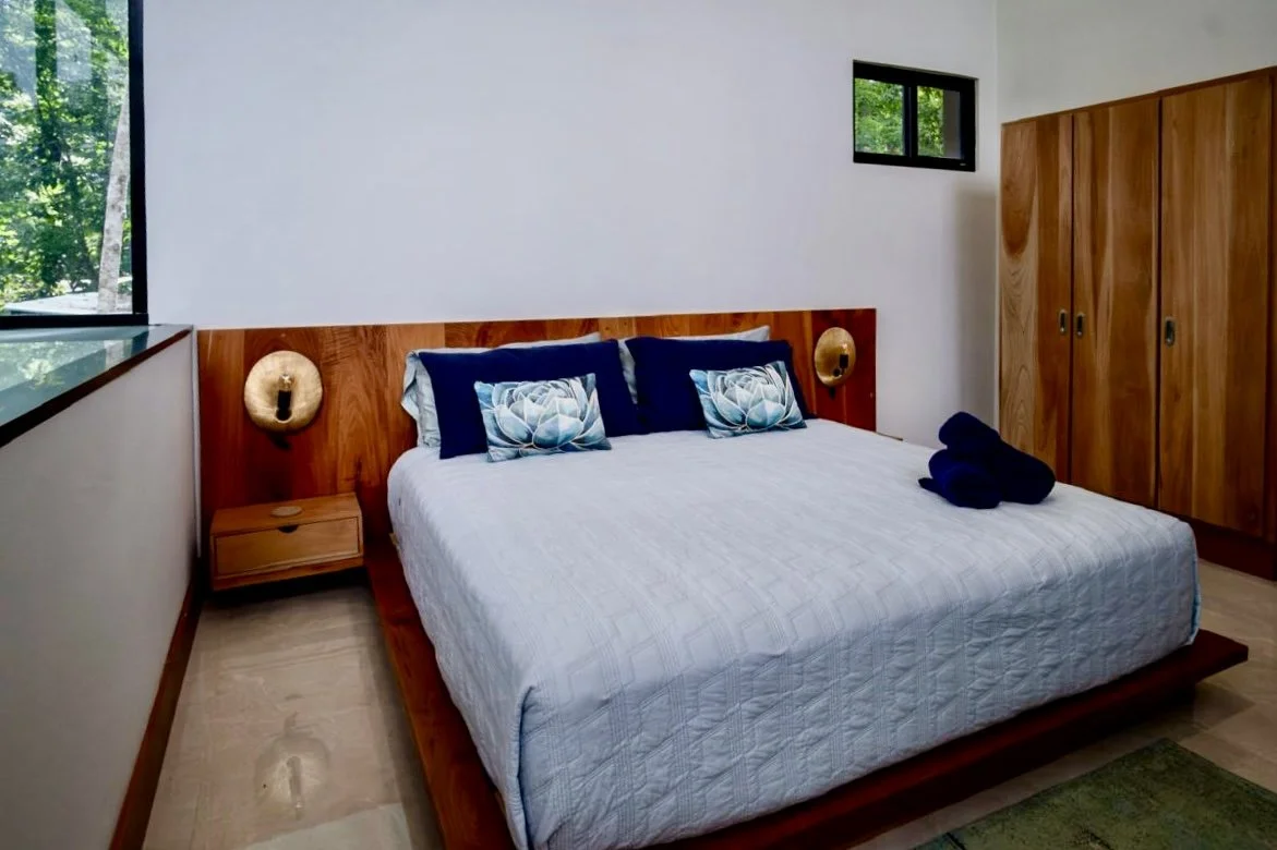 Spacious bedroom with wooden platform bed, custom built-in wardrobes and natural light at House of Light in Paquera, Costa Rica