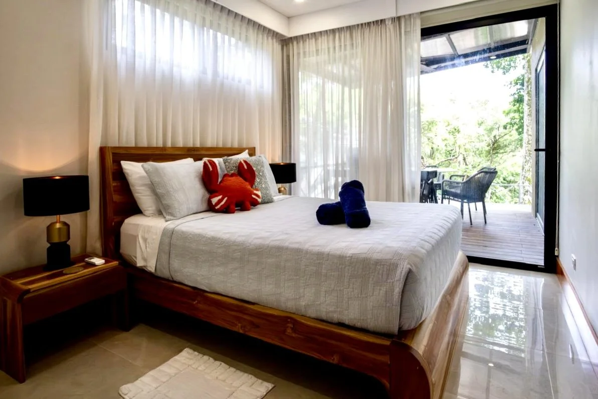 Bright furnished bedroom with wooden bed and sliding glass doors opening onto a private tropical terrace at House of Light in Paquera, Costa Rica