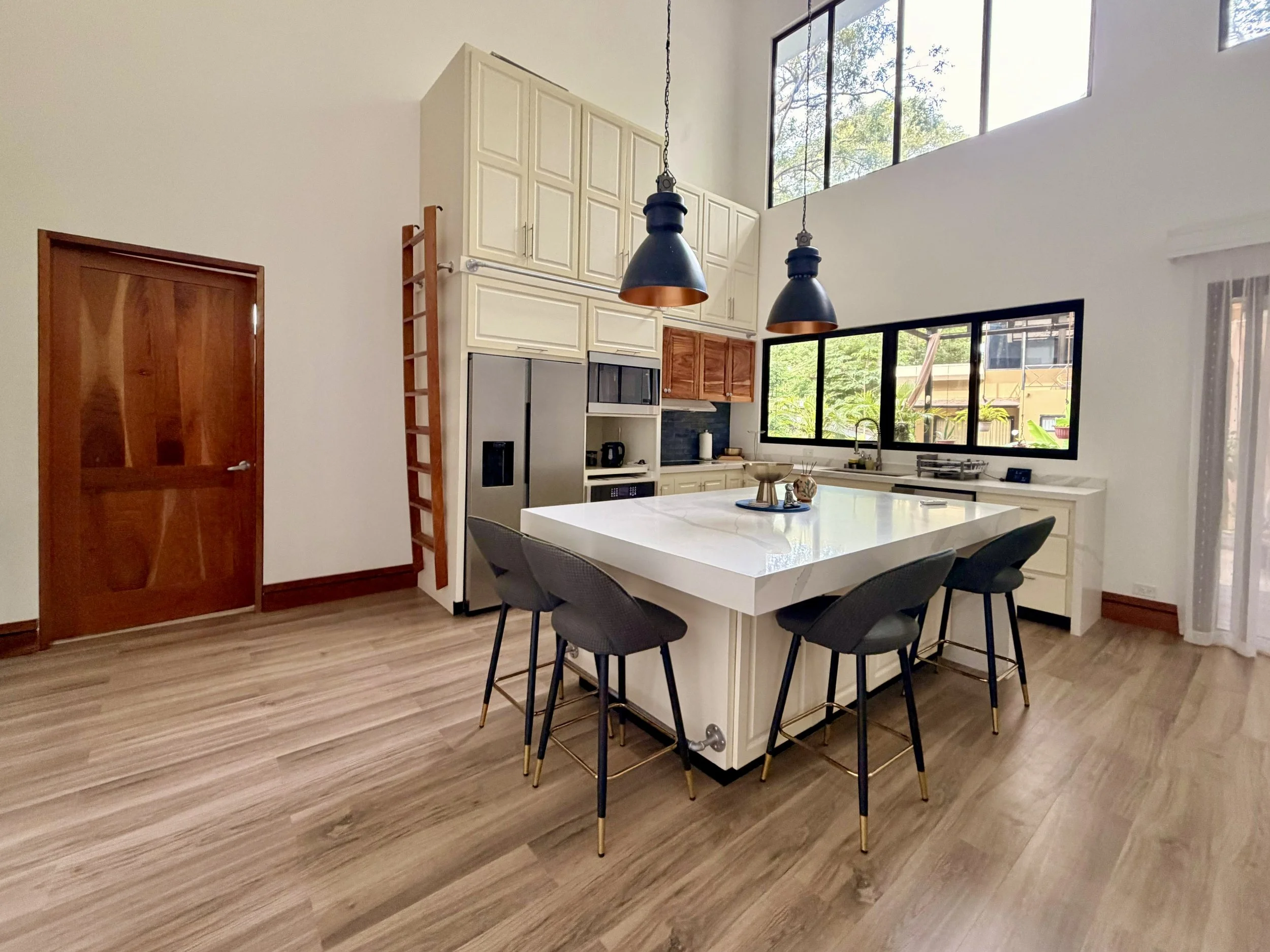 Casa Quantum open-concept kitchen with high ceilings, white cabinetry and large windows overlooking greenery.