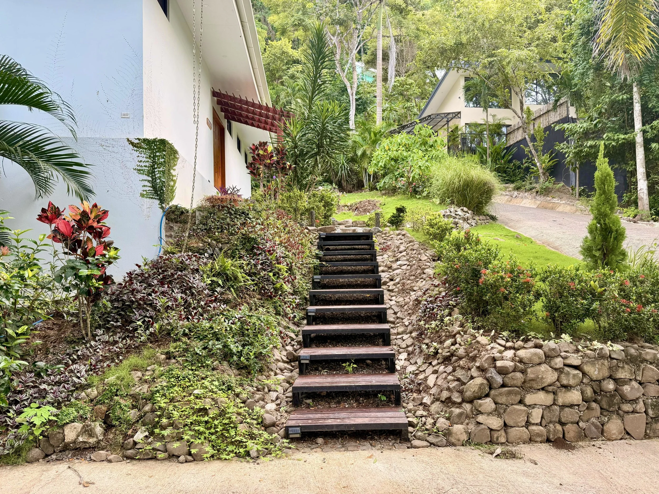 Casa Quantum tropical garden walkway with wooden steps, stone landscaping and lush greenery in Paquera, Costa Rica.