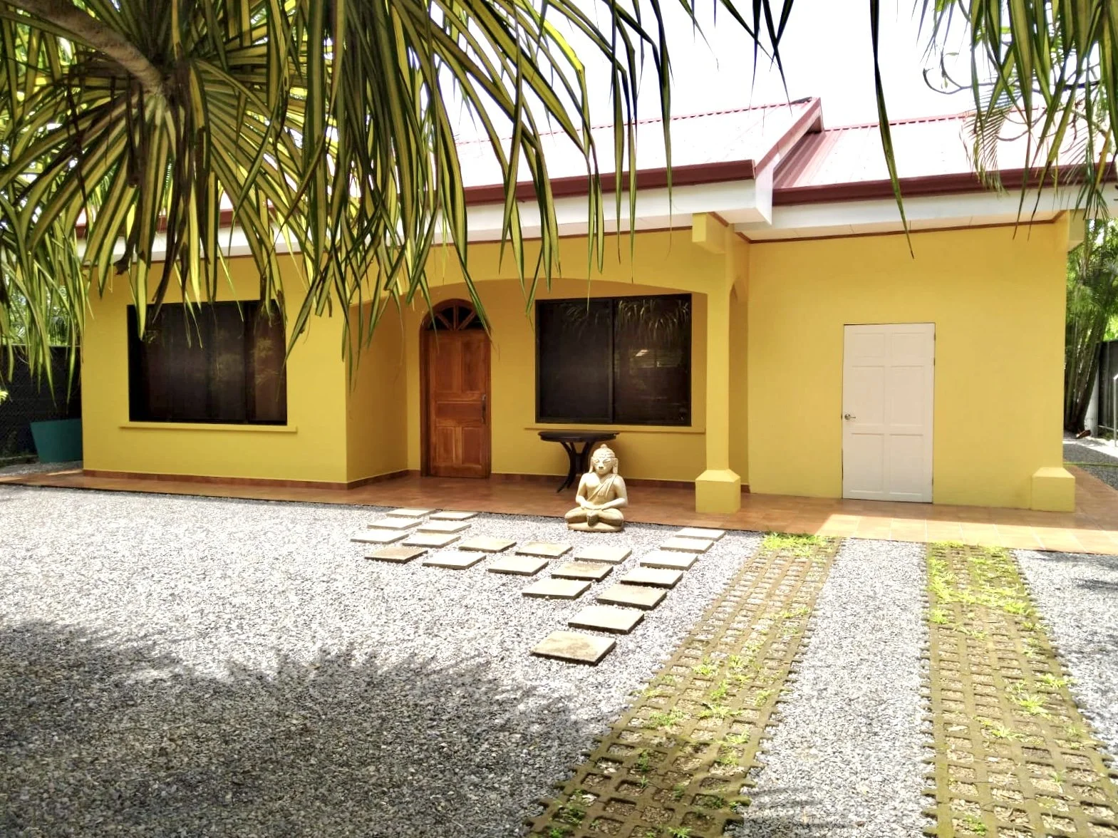 Front courtyard of Casa Palma Bonita with tropical palm trees, gravel landscaping and stepping-stone walkway