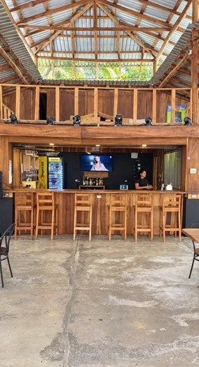 Wooden bar counter with seating and television at restaurant and bar for sale in Tambor, Costa Rica.