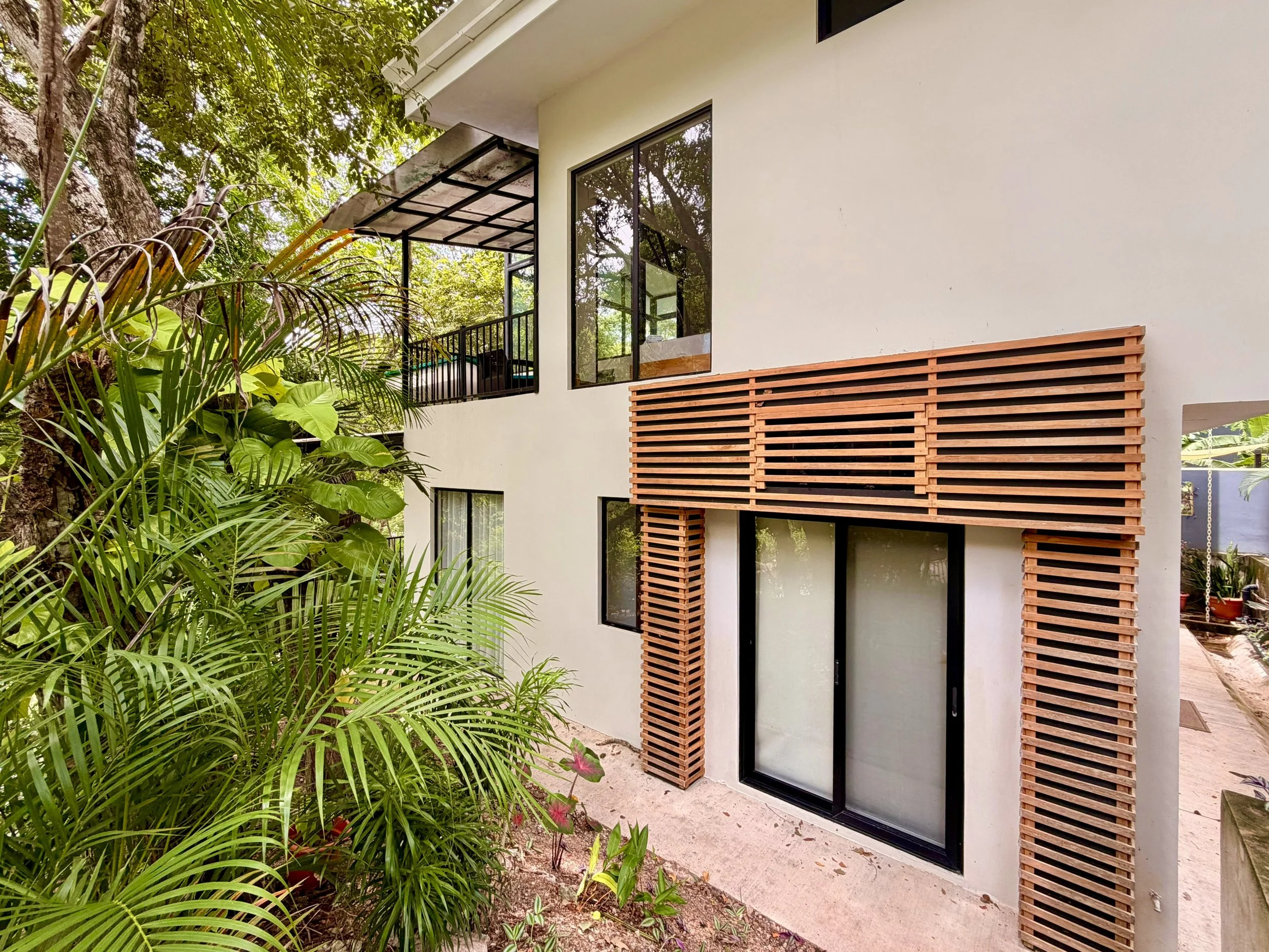 Casa Colina modern two-story exterior with wooden privacy screens, large windows and tropical plants.