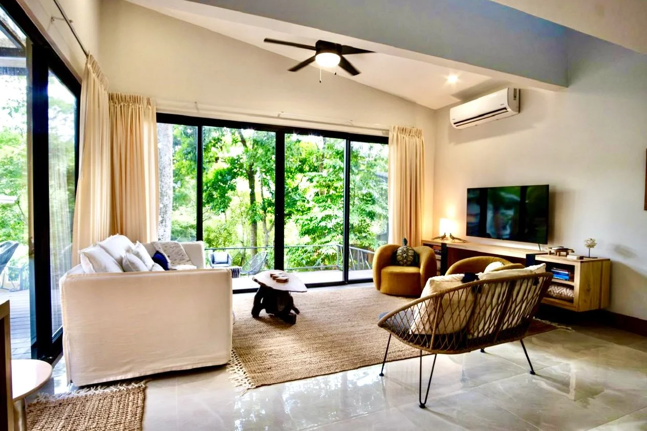 Spacious furnished living room with ceiling fan, comfortable seating and large windows overlooking tropical gardens at House of Light in Paquera, Costa Rica