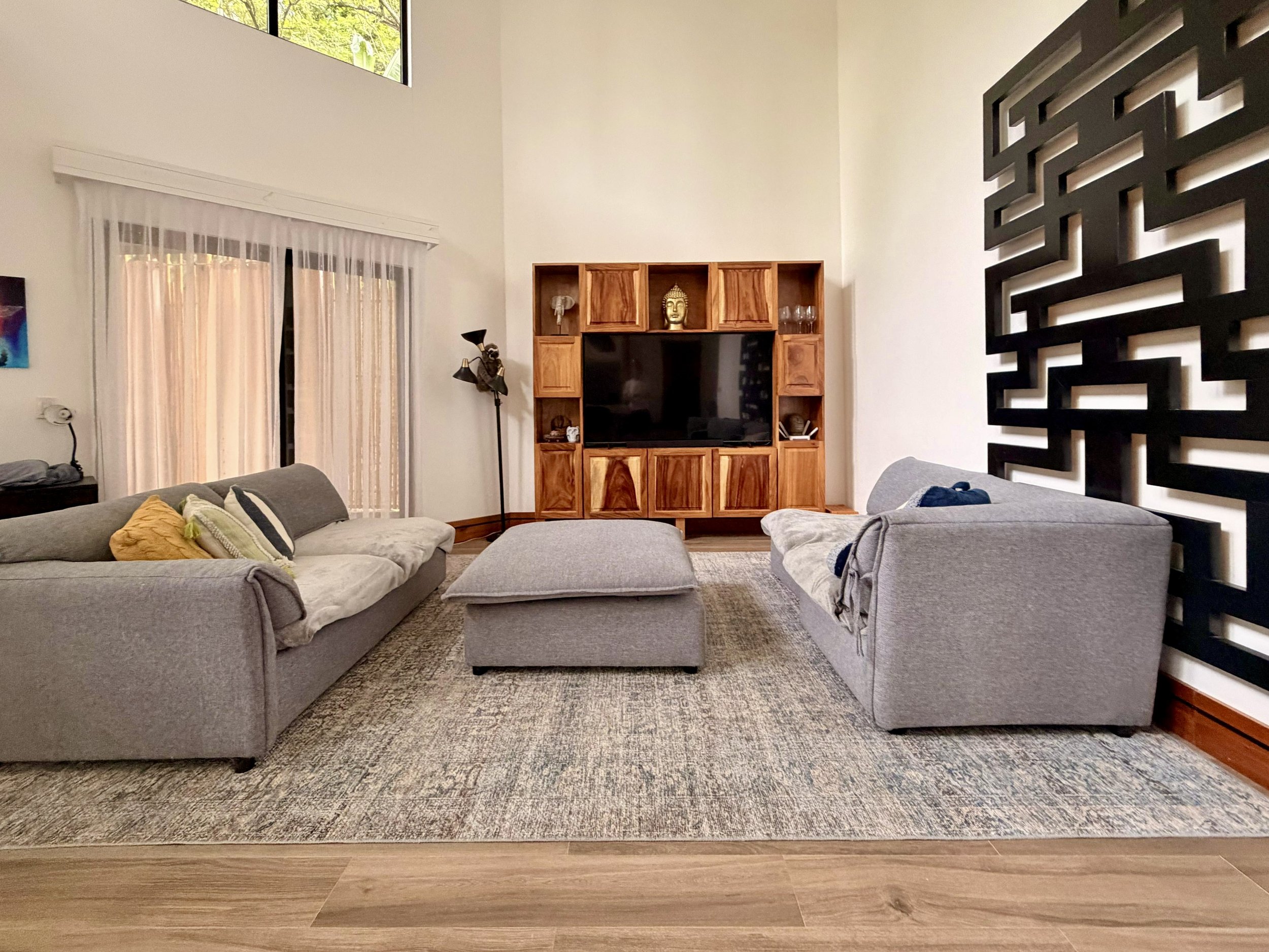 Casa Quantum furnished living room with comfortable sofas, large ottoman and wooden entertainment cabinet.