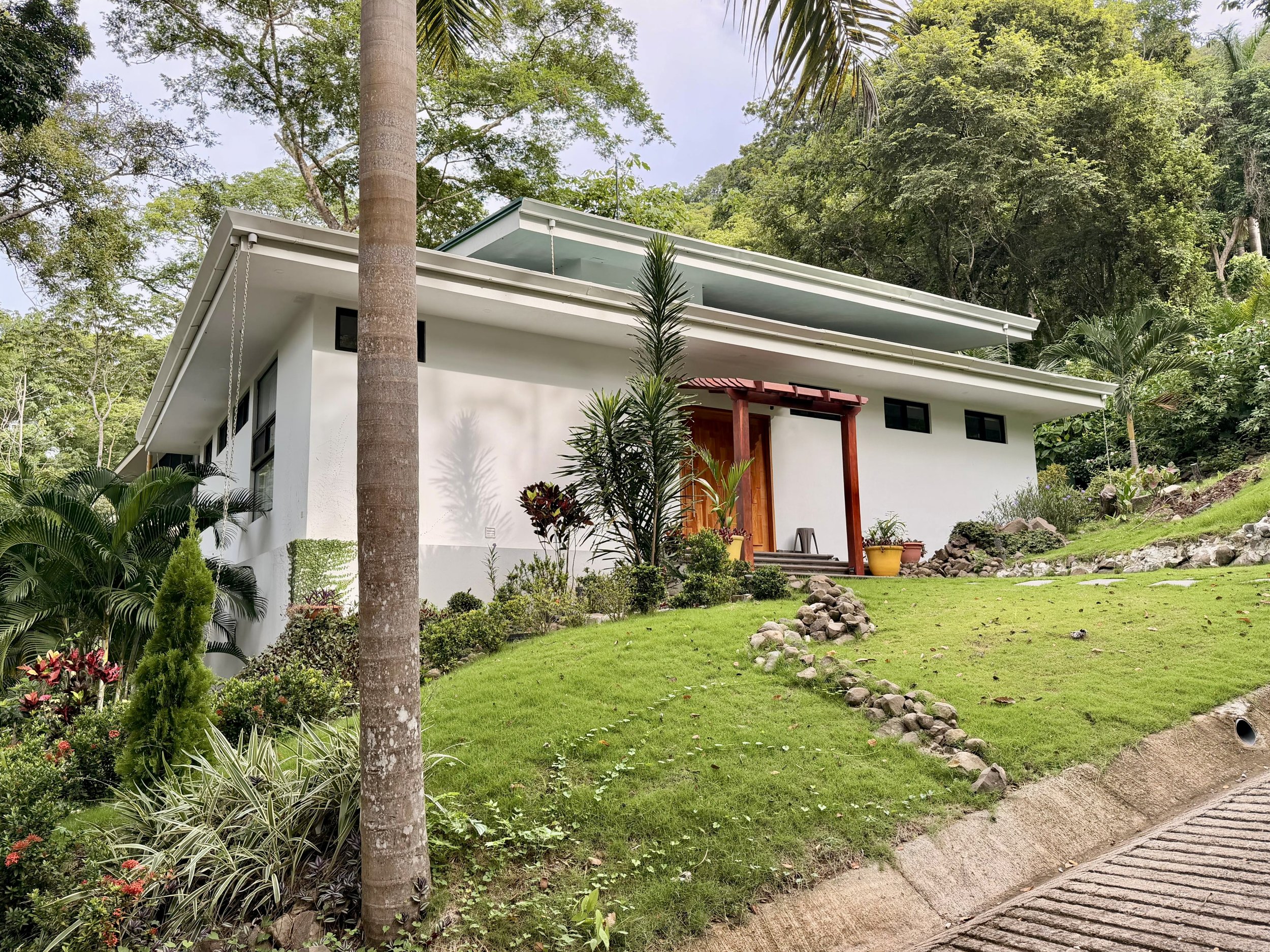 Casa Quantum modern white exterior with lush green lawn, mature trees and tropical landscaping.