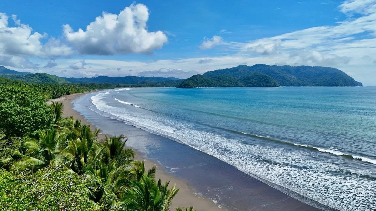 Panoramic view of Tambor Beach with turquoise Pacific waters, sandy shoreline and green tropical hills.