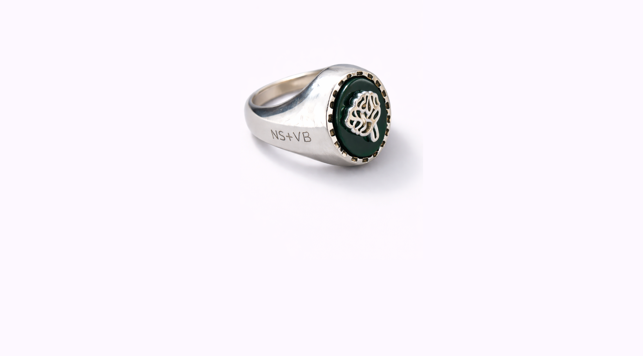 Close-up of a silver ring with a green oval centerpiece featuring a silver lion's head emblem and the inscription 'NS4VB' engraved on the band, shot against a white background.